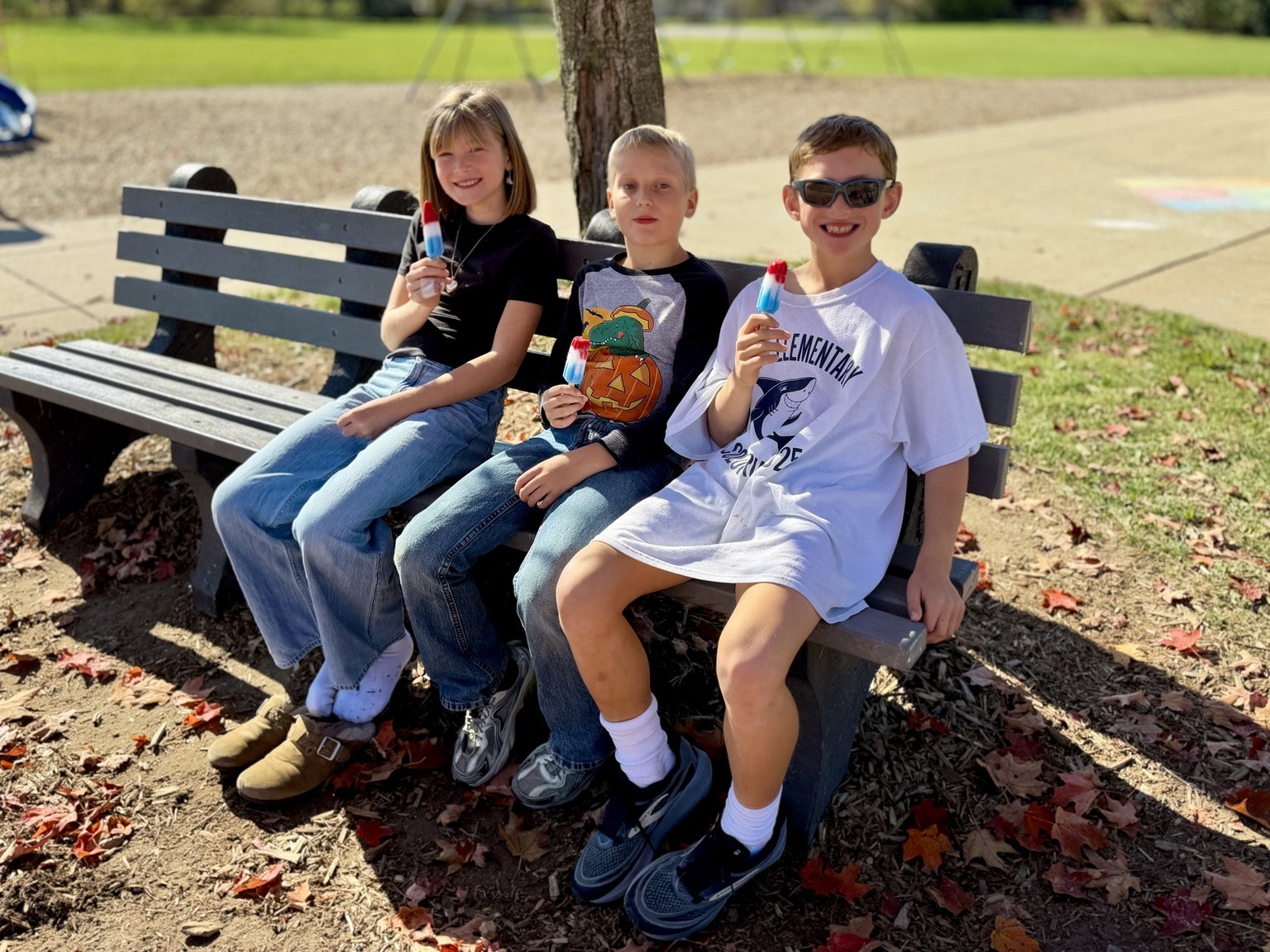 Three classmates enjoying frozen treats on an outdoor bench.