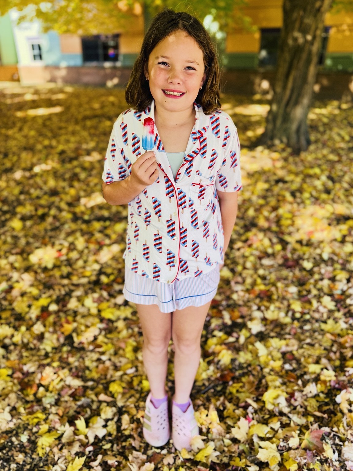 A student smiling with a frozen treat beneath an autumn tree.