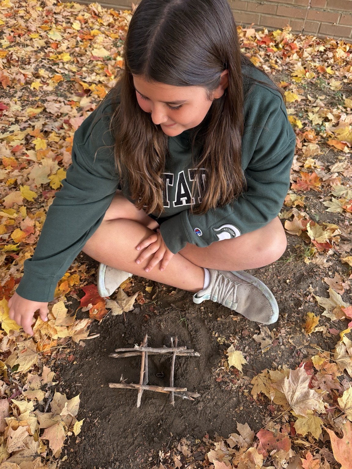 A student sitting beside a small grid made with sticks on the ground.